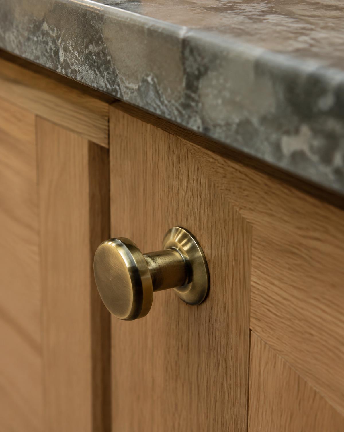 Muted brass knob on a natural oak cabinet door